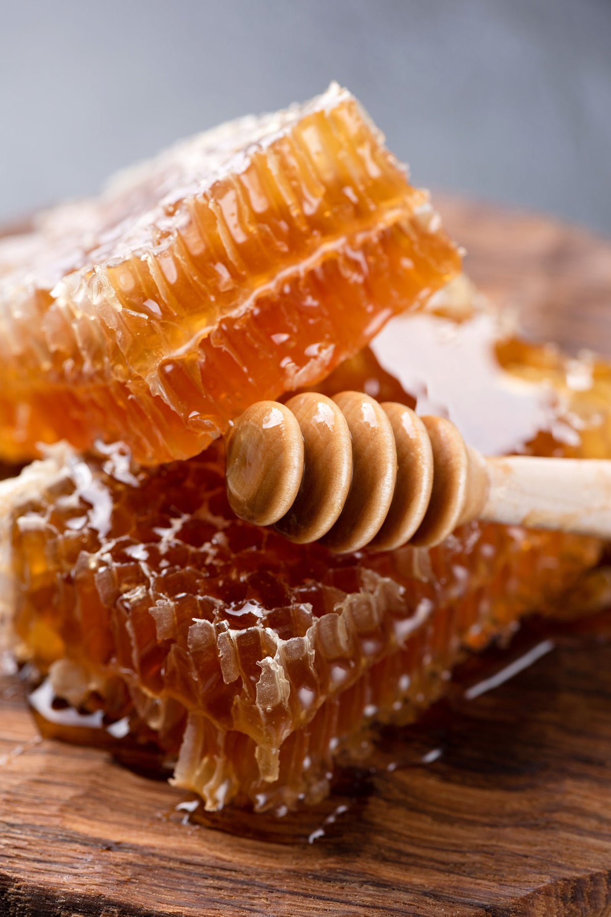 Honeycomb with honey and a honey dipper on a wooden surface