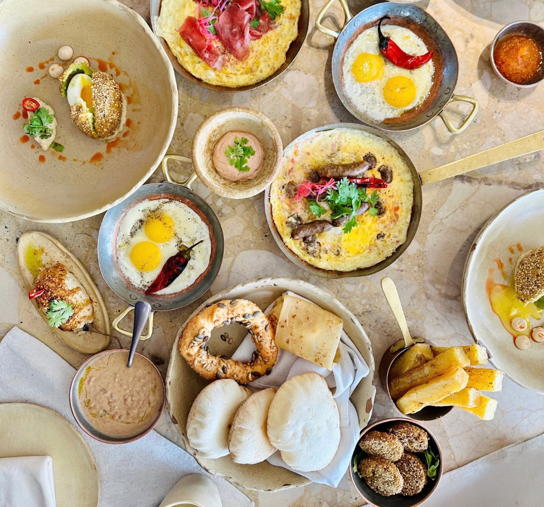Assorted breakfast dishes including eggs, bread, and sauces on a textured surface.