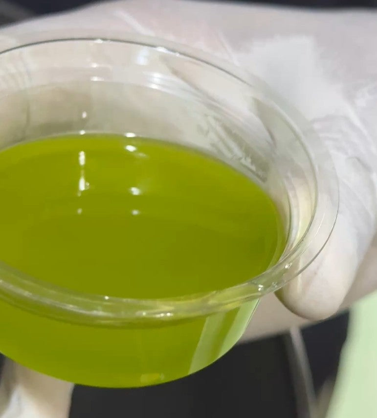 Clear container with yellow-green olive oil liquid held by a gloved hand